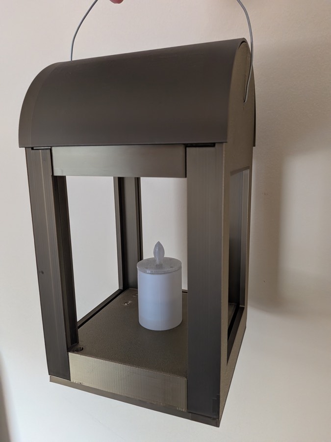 A finished lantern hanging by its wire handle: printed housing with open windows and the candle unit on its base plate